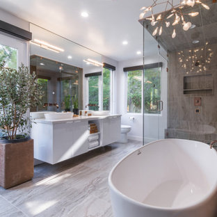 Large trendy brown tile and porcelain tile porcelain tile, beige floor and double-sink freestanding bathtub photo in Los Angeles with flat-panel cabinets, white cabinets, a one-piece toilet, white walls, a vessel sink, solid surface countertops, a hinged shower door, white countertops, a niche and a floating vanity