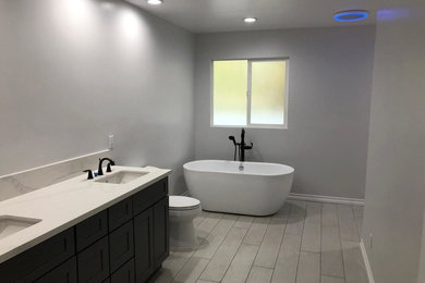 ロサンゼルスにあるお手頃価格の広いモダンスタイルのおしゃれなマスターバスルーム (分離型トイレ、グレーの壁、セラミックタイルの床、クオーツストーンの洗面台、グレーの床、開き戸のシャワー、白い洗面カウンター) の写真