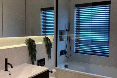 Photo of a small contemporary family bathroom in Edinburgh with flat-panel cabinets, brown cabinets, a built-in bath, a shower/bath combination, a wall mounted toilet, grey tiles, ceramic tiles, grey walls, ceramic flooring, a built-in sink, grey floors and a hinged door.
