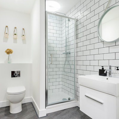 Corner shower - scandinavian white tile and subway tile dark wood floor and gray floor corner shower idea in Dorset with flat-panel cabinets, white cabinets, a one-piece toilet, white walls and a wall-mount sink