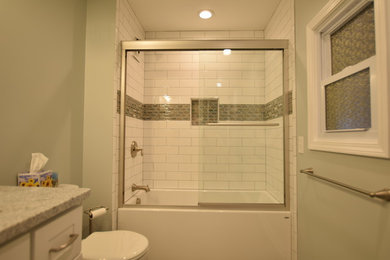 ニューヨークにある高級な中くらいなトランジショナルスタイルのおしゃれなバスルーム (浴槽なし) (シェーカースタイル扉のキャビネット、白いキャビネット、アルコーブ型浴槽、シャワー付き浴槽	、分離型トイレ、白いタイル、サブウェイタイル、緑の壁、磁器タイルの床、アンダーカウンター洗面器、クオーツストーンの洗面台、グレーの床、引戸のシャワー) の写真