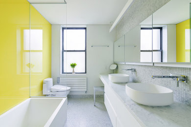 Immagine di una stanza da bagno minimal con ante lisce, ante bianche, vasca ad angolo, vasca/doccia, WC monopezzo, piastrelle multicolore, pareti gialle, pavimento con piastrelle a mosaico, lavabo a bacinella e top in marmo