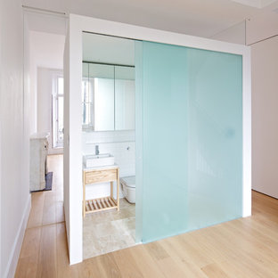 Modelo de cuarto de baño vestidor, minimalista, con lavabo sobreencimera, puertas de armario de madera clara, baldosas y/o azulejos blancos, baldosas y/o azulejos de cemento, paredes blancas, suelo de madera clara, sanitario de una pieza y armarios abiertos