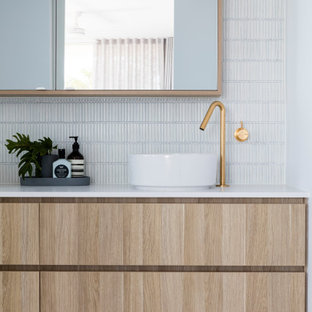 Photo of a beach style bathroom in Sunshine Coast with flat-panel cabinets, light wood cabinets, white tile, mosaic tile, white walls, pebble tile floors, a vessel sink, grey floor, white benchtops and a floating vanity.