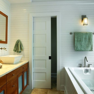 Example of a mid-sized beach style master travertine floor drop-in bathtub design in New York with shaker cabinets, medium tone wood cabinets, limestone countertops, a vessel sink and white walls