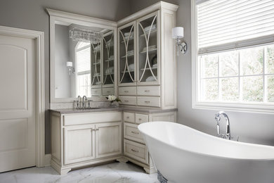 Photo of a large classic ensuite bathroom in Louisville with recessed-panel cabinets, white cabinets, a claw-foot bath, grey walls, marble flooring, a submerged sink and grey floors.