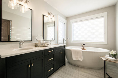 This is an example of a medium sized traditional ensuite bathroom in Calgary with recessed-panel cabinets, black cabinets, a freestanding bath, an alcove shower, grey tiles, porcelain tiles, grey walls, porcelain flooring, a submerged sink, engineered stone worktops, grey floors and a hinged door.