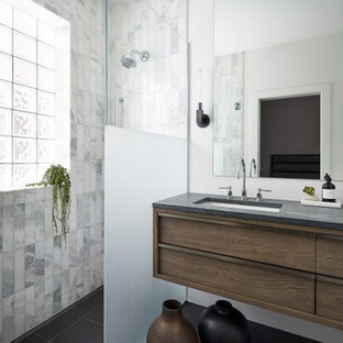 This is an example of a mid-sized contemporary master bathroom in Chicago with flat-panel cabinets, medium wood cabinets, a curbless shower, white tile, marble, white walls, slate floors, an undermount sink, limestone benchtops, black floor, a hinged shower door and grey benchtops.