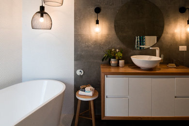 Modelo de cuarto de baño actual con bañera exenta, baldosas y/o azulejos blancos, paredes grises y lavabo sobreencimera