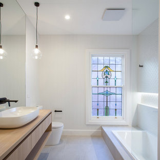 Inspiration for a contemporary 3/4 bathroom with a drop-in tub, white tile, white walls, grey floor, flat-panel cabinets, light wood cabinets, a one-piece toilet, a vessel sink, wood benchtops and beige benchtops.
