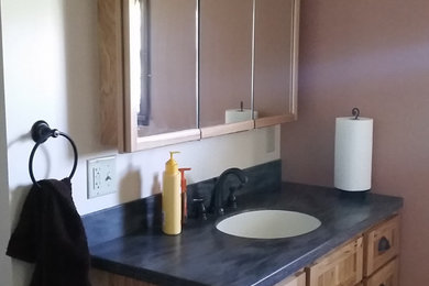 Cette image montre une salle d'eau traditionnelle en bois vieilli de taille moyenne avec un placard avec porte à panneau encastré, WC séparés, un mur beige, un lavabo encastré, un plan de toilette en stéatite et un plan de toilette gris.