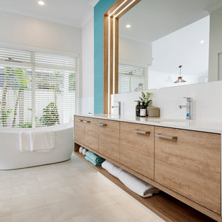 Design ideas for a beach style master bathroom in Perth with flat-panel cabinets, light wood cabinets, a freestanding tub, blue tile, blue walls, a wall-mount sink, white floor and white benchtops.