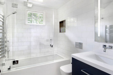 Стильный дизайн: ванная комната среднего размера в стиле модернизм с плоскими фасадами, синими фасадами, полновстраиваемой ванной, душем над ванной, инсталляцией, белой плиткой, мраморной плиткой, белыми стенами, полом из мозаичной плитки, врезной раковиной, мраморной столешницей, серым полом, душем с распашными дверями и белой столешницей - последний тренд