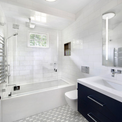Inspiration for a mid-sized modern white tile and marble tile mosaic tile floor and gray floor tub/shower combo remodel in New York with flat-panel cabinets, blue cabinets, an undermount tub, a wall-mount toilet, white walls, an undermount sink, marble countertops, a hinged shower door and white countertops