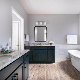 Elegant white tile medium tone wood floor and brown floor freestanding bathtub photo in Other with shaker cabinets, blue cabinets, gray walls, an undermount sink and beige countertops