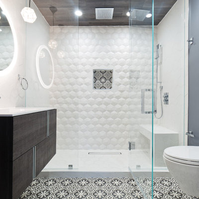 Trendy 3/4 white tile multicolored floor alcove shower photo in San Francisco with flat-panel cabinets, dark wood cabinets, a wall-mount toilet, gray walls, an integrated sink, a hinged shower door and white countertops