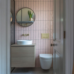 Bild på ett funkis beige beige badrum, med släta luckor, skåp i ljust trä, rosa kakel, ett fristående handfat, träbänkskiva och grått golv