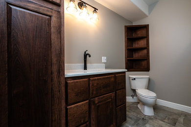 Diseño de cuarto de baño clásico de tamaño medio con armarios con paneles lisos, puertas de armario marrones, sanitario de dos piezas, paredes grises, aseo y ducha, encimera de acrílico, encimeras blancas y lavabo bajoencimera