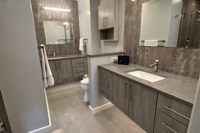 This is an example of a medium sized contemporary ensuite bathroom in DC Metro with flat-panel cabinets, grey cabinets, an alcove shower, a two-piece toilet, grey tiles, porcelain tiles, grey walls, porcelain flooring, a submerged sink, engineered stone worktops, grey floors, a hinged door, grey worktops, a shower bench, double sinks and a floating vanity unit.
