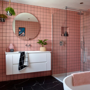 Inspiration for a contemporary bathroom in London with flat-panel cabinets, white cabinets, a freestanding bath, a corner shower, pink tiles, pink walls, an integrated sink, black floors, a sliding door and white worktops.