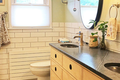 Photo of a large modern ensuite bathroom in Baltimore with freestanding cabinets, light wood cabinets, a built-in bath, a shower/bath combination, a two-piece toilet, white tiles, porcelain tiles, green walls, porcelain flooring, a submerged sink, soapstone worktops, grey floors, a shower curtain and black worktops.