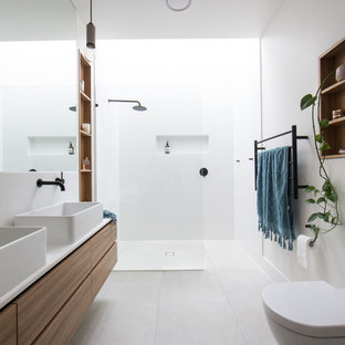 Photo of a contemporary bathroom in Melbourne with flat-panel cabinets, medium wood cabinets, a curbless shower, white tile, white walls, a vessel sink, grey floor, an open shower and white benchtops.