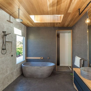 This is an example of a contemporary master wet room bathroom in Gold Coast - Tweed with flat-panel cabinets, black cabinets, a freestanding tub, black tile, gray tile, mosaic tile, mosaic tile floors, a vessel sink, wood benchtops, black floor and an open shower.