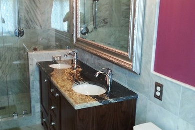 Mid-sized elegant 3/4 marble floor and white floor alcove shower photo with a one-piece toilet, pink walls, an undermount sink, a hinged shower door, recessed-panel cabinets, dark wood cabinets and granite countertops