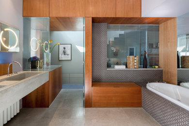 Large contemporary bathroom in London with flat-panel cabinets, medium wood cabinets, a built-in bath, grey tiles, cement tiles, limestone flooring, limestone worktops, grey walls, an integrated sink and feature lighting.