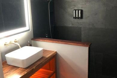 Doorless shower - small modern 3/4 black tile and slate tile single-sink doorless shower idea in Hawaii with medium tone wood cabinets, a two-piece toilet, a vessel sink, wood countertops and a freestanding vanity