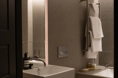 Medium sized modern bathroom in London with raised-panel cabinets, a built-in bath, a wall mounted toilet, green tiles, ceramic tiles, grey walls, ceramic flooring, a wall-mounted sink, beige floors and a hinged door.
