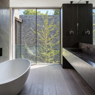 Modern bathroom in London with a freestanding bath, dark hardwood flooring, a trough sink, brown floors, grey worktops, a wall niche, double sinks and a floating vanity unit.