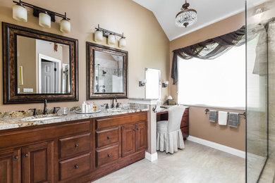 Example of a large transitional master beige tile and porcelain tile porcelain tile and beige floor corner shower design in Indianapolis with raised-panel cabinets, medium tone wood cabinets, beige walls, an undermount sink, granite countertops, a hinged shower door and multicolored countertops