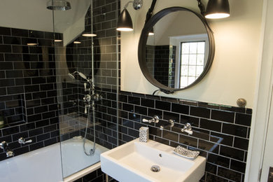 This is an example of a small contemporary family bathroom in London with a built-in bath, a shower/bath combination, a one-piece toilet, black tiles, metro tiles, white walls, porcelain flooring and a pedestal sink.
