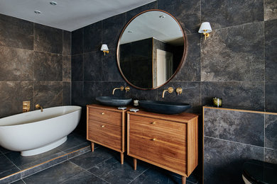 Design ideas for a medium sized contemporary bathroom in London with flat-panel cabinets, medium wood cabinets, a freestanding bath, black tiles, a vessel sink, wooden worktops, black floors and brown worktops.