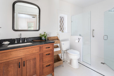 Design ideas for a medium sized classic ensuite bathroom in Boston with flat-panel cabinets, medium wood cabinets, an alcove shower, a one-piece toilet, white tiles, ceramic tiles, white walls, porcelain flooring, a submerged sink, soapstone worktops, white floors, a hinged door and black worktops.