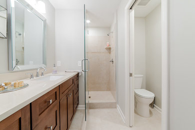 Medium sized classic shower room bathroom in Minneapolis with shaker cabinets, medium wood cabinets, an alcove shower, a two-piece toilet, beige tiles, travertine tiles, white walls, travertine flooring, a submerged sink, engineered stone worktops, beige floors and a hinged door.