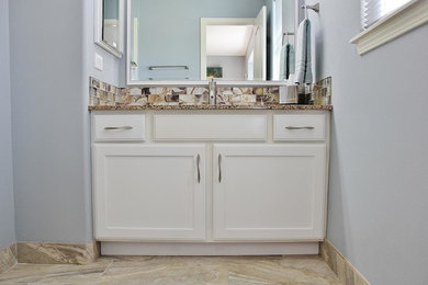 Example of a mid-sized beach style 3/4 beige tile, brown tile, white tile and stone slab ceramic tile bathroom design in Orange County with raised-panel cabinets, white cabinets, a one-piece toilet, blue walls, a drop-in sink and granite countertops