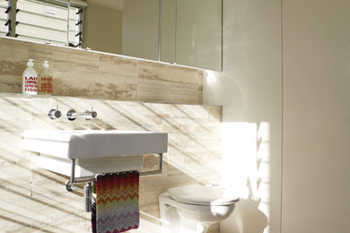 Idéer för mellanstora medelhavsstil badrum, med luckor med upphöjd panel, en vägghängd toalettstol, beige kakel, stenkakel, vita väggar, travertin golv, ett väggmonterat handfat och kaklad bänkskiva