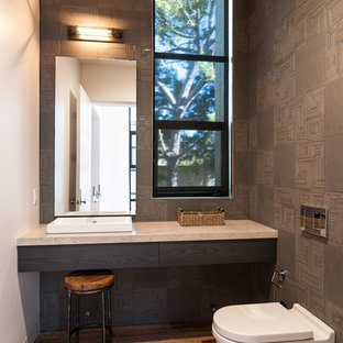 Modelo de cuarto de baño con ducha, moderno, de tamaño medio, con baldosas y/o azulejos de porcelana, armarios con paneles lisos, puertas de armario negras, bidé, paredes grises, suelo de madera clara, lavabo encastrado y encimera de granito
