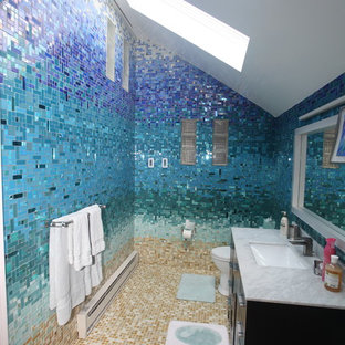 Example of a large island style master blue tile and glass tile ceramic tile and beige floor bathroom design in New York with flat-panel cabinets, black cabinets, a one-piece toilet, blue walls, a pedestal sink and solid surface countertops