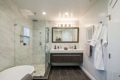 Mid-sized transitional master porcelain tile and gray floor bathroom photo in Los Angeles with flat-panel cabinets, distressed cabinets, a two-piece toilet, white walls, a hinged shower door, an integrated sink, quartzite countertops and white countertops