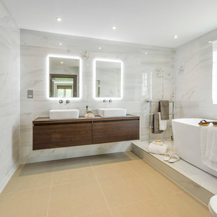 Inspiration for a contemporary ensuite bathroom in London with a freestanding bath, a built-in shower, flat-panel cabinets, dark wood cabinets, a one-piece toilet, grey tiles, grey walls, a vessel sink, wooden worktops, a hinged door and brown worktops.
