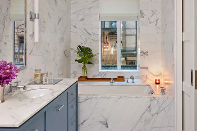 Bathroom - mid-sized contemporary master white tile and stone slab white floor bathroom idea in New York with an undermount sink, flat-panel cabinets, blue cabinets, an undermount tub, white walls, marble countertops and white countertops