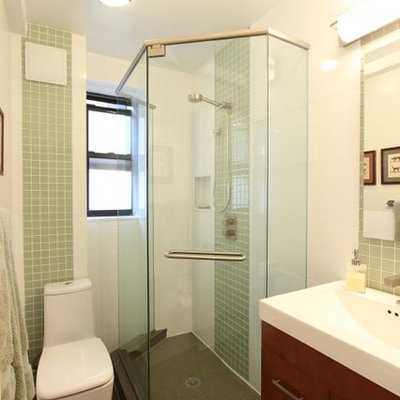 Corner shower - small eclectic 3/4 green tile and porcelain tile porcelain tile corner shower idea in New York with flat-panel cabinets, medium tone wood cabinets, a one-piece toilet, white walls, a trough sink and solid surface countertops