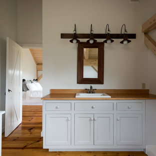 Mid-sized farmhouse master light wood floor and yellow floor bathroom photo in New York with recessed-panel cabinets, white cabinets, white walls and wood countertops