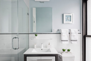 Corner shower - small contemporary 3/4 white tile and ceramic tile porcelain tile and black floor corner shower idea in New York with flat-panel cabinets, white cabinets, a two-piece toilet, blue walls, an integrated sink, quartz countertops and a hinged shower door