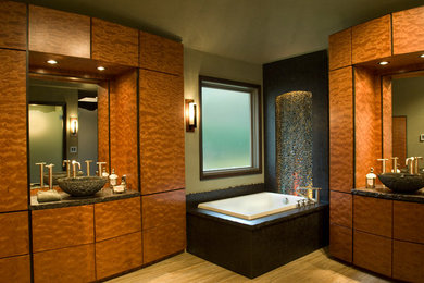 Ejemplo de cuarto de baño principal contemporáneo grande con armarios tipo mueble, lavabo sobreencimera, puertas de armario de madera oscura, encimera de granito, bañera esquinera, paredes beige y suelo de madera clara