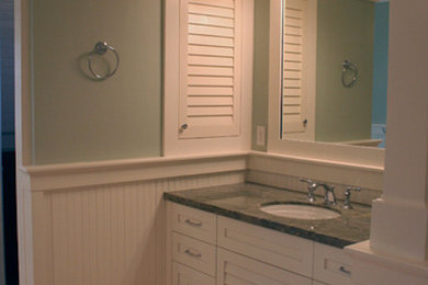 Aménagement d'une salle de bain avec des portes de placard blanches, un plan de toilette en granite, un carrelage beige et un mur vert.