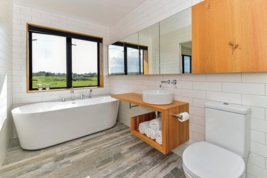Modelo de cuarto de baño principal moderno de tamaño medio con armarios abiertos, bañera exenta, paredes blancas, encimera de madera y lavabo sobreencimera